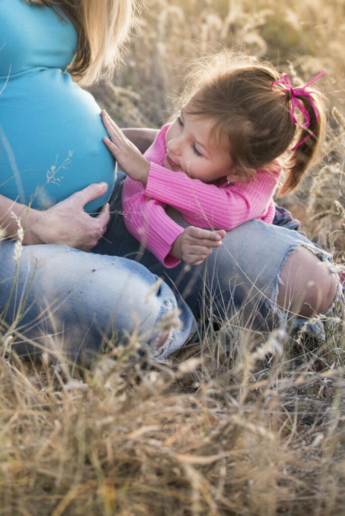 Pregnant woman with child sharing a tender moment in a grassy field.